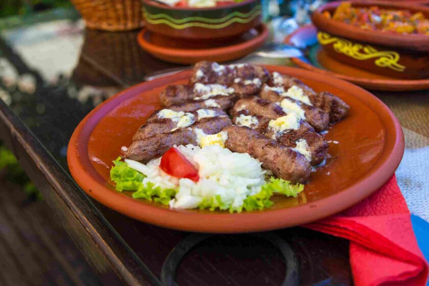 Tanjir sa ćevapima, sirom, lukom i povrćem u tradicionalnoj posudi